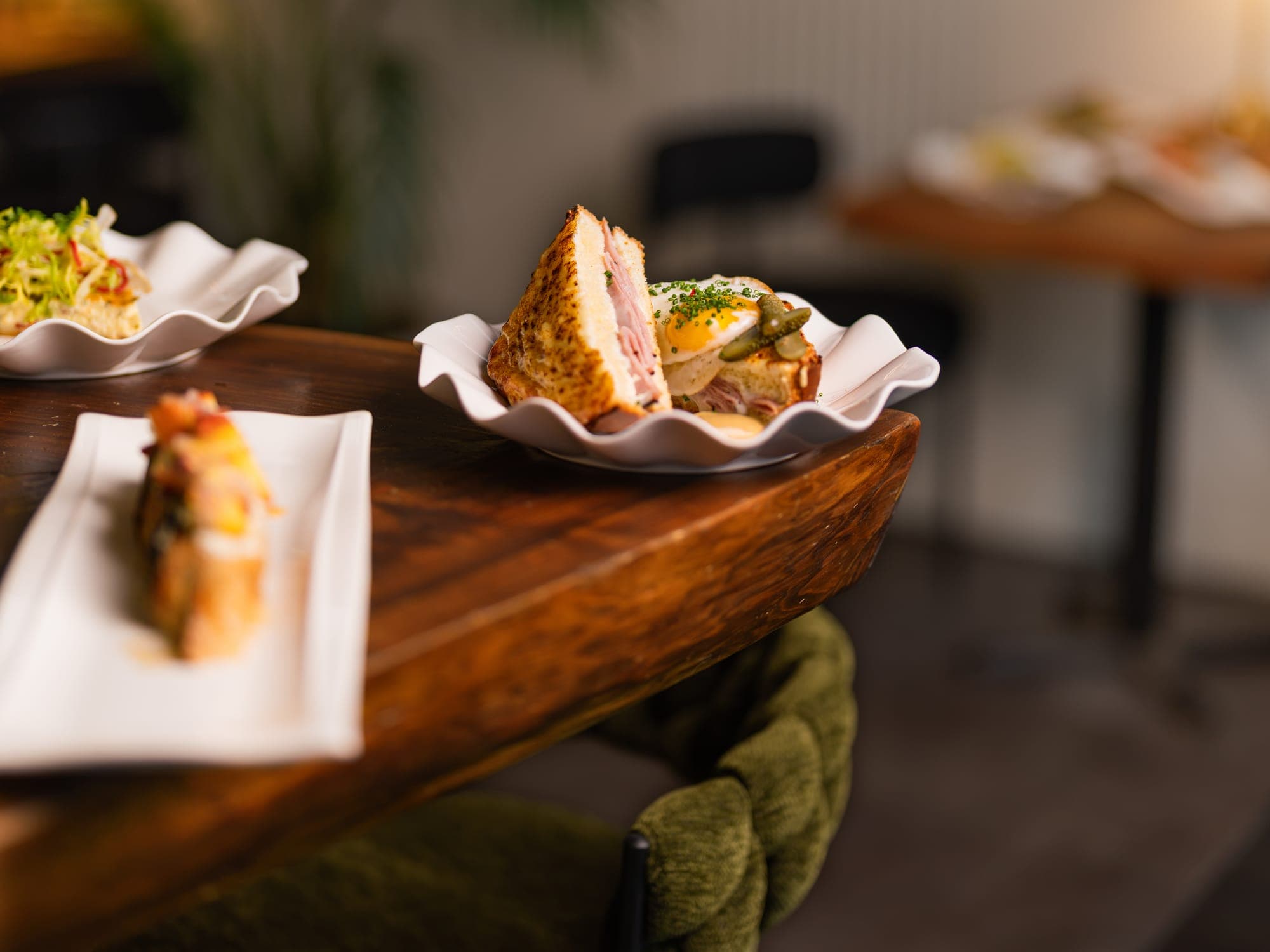 A plated dish on the redwood bar at Chariot Gathering House, with a moss-velvet chair beneath the table's edge.